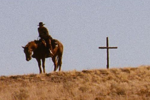 Cowboy on horseback with a cross in the desert